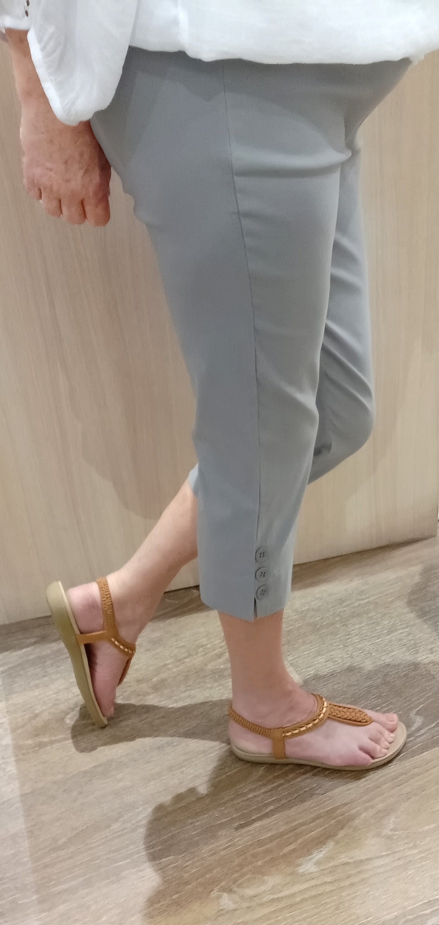 Woman wearing silver SSF Button Pants with a white Gypsy Top and brown thongs near Boo Boo's counter