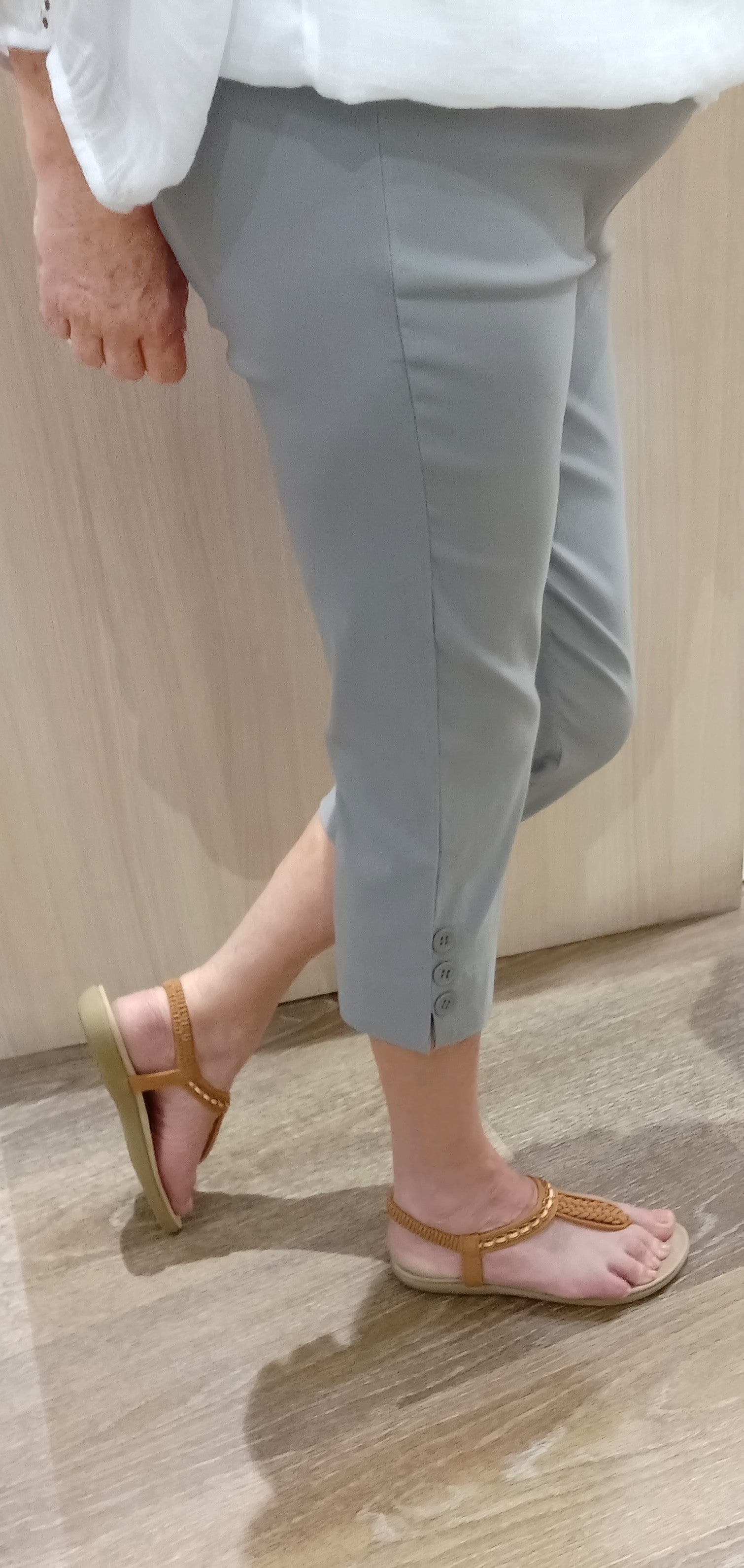 Woman wearing silver SSF Button Pants with a white Gypsy Top and brown thongs near Boo Boo's counter