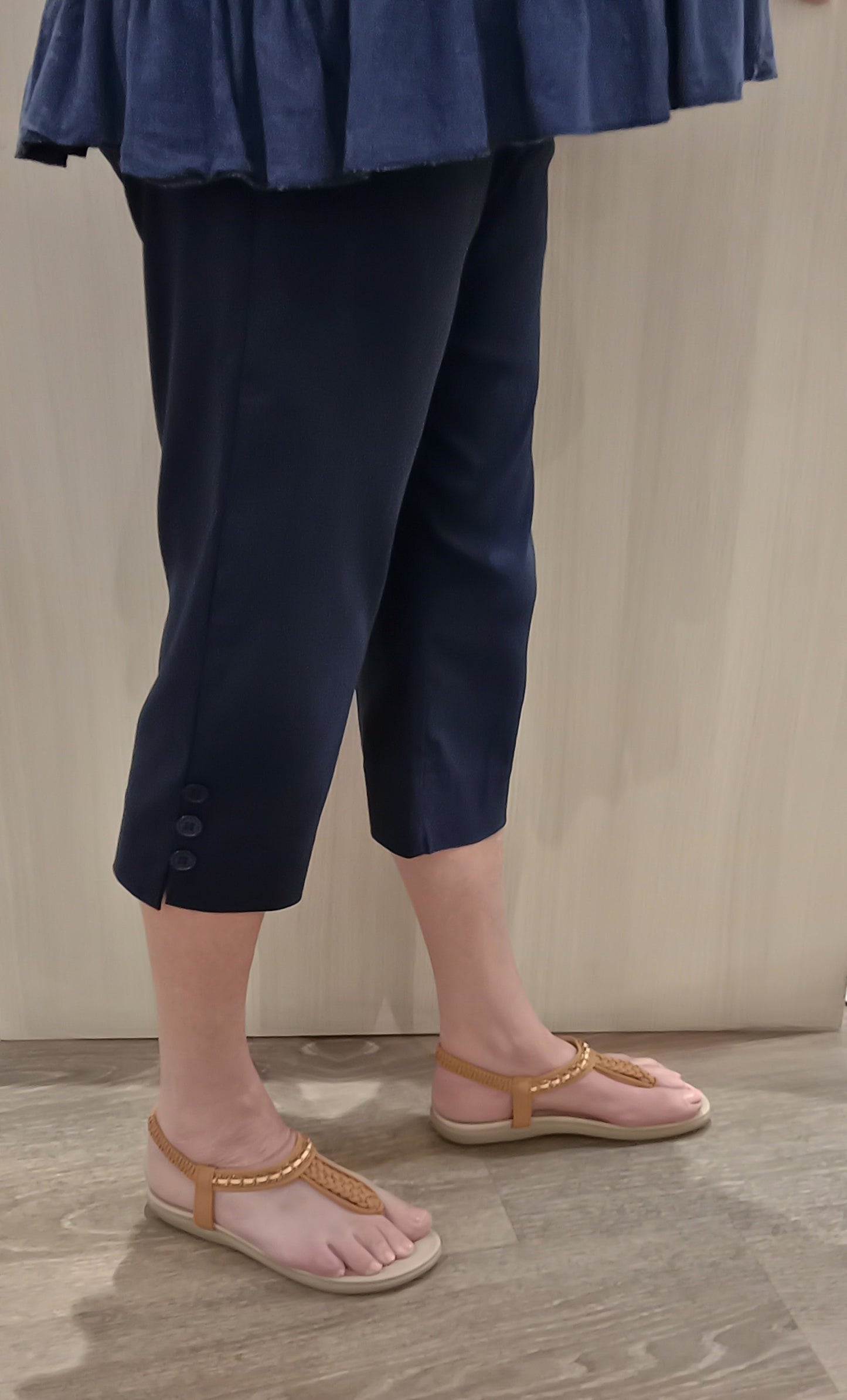 Woman wearing navy SSF Button Pants with a white navy top and brown thongs near Boo Boo's counter