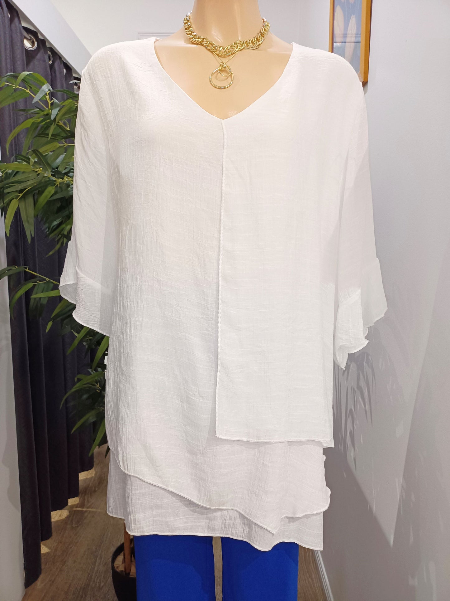 A white frill sleeve, layered Split Top on a mannequin with gold necklace and royal blue SSF Button Pants against Boo's Boo's shop wall.