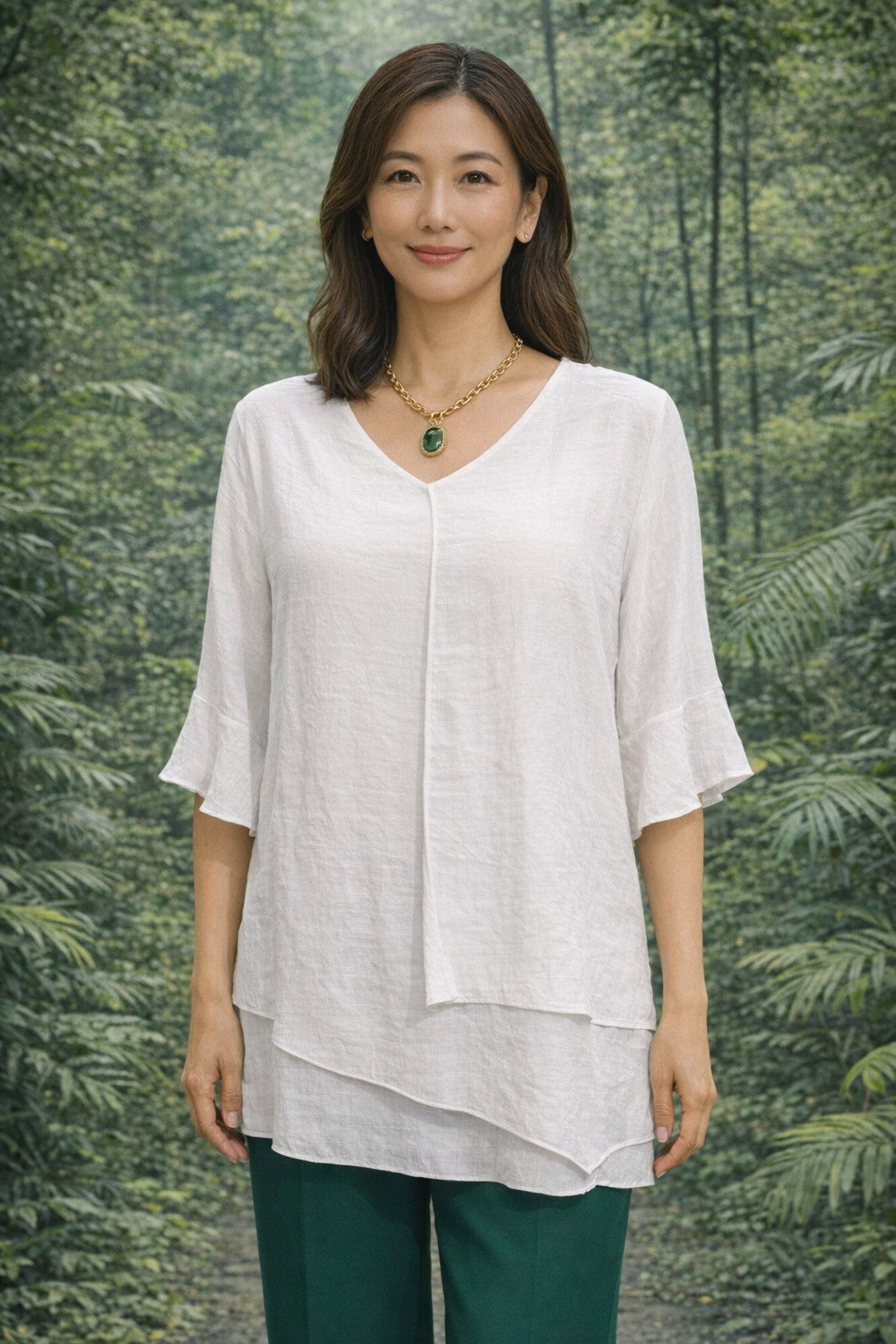 Woman wearing a white Split Top and green pants standing in front of a forest background
