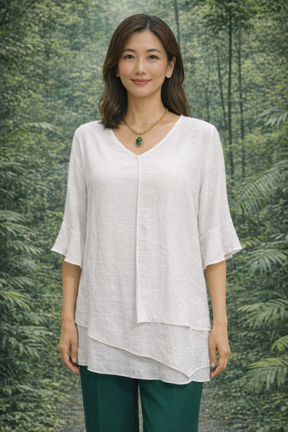 Woman wearing a white Split Top and green pants standing in front of a forest background